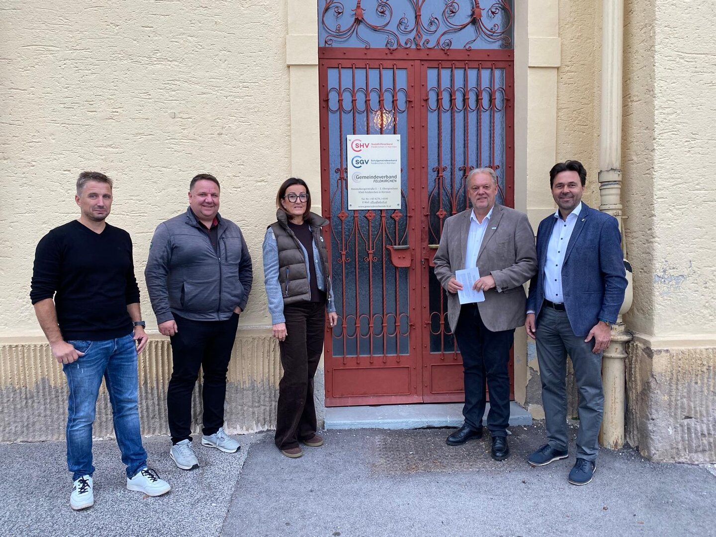 Fünf Personen stehen vor einem Gebäude mit roter Tür in Feldkirchen.