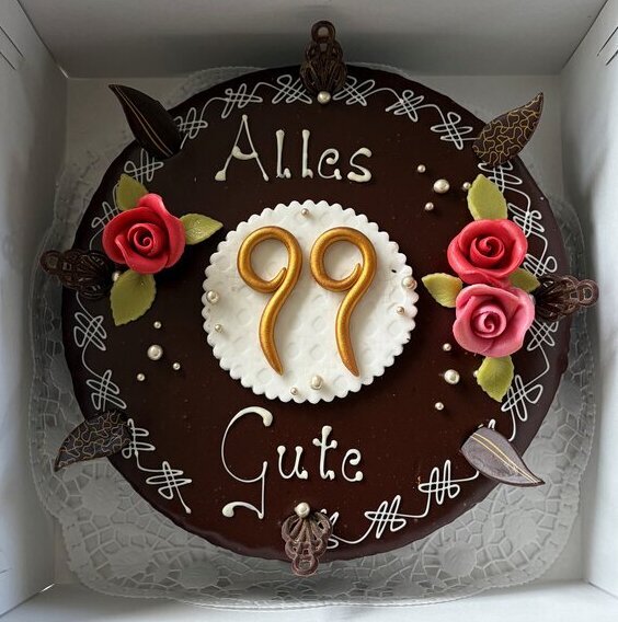 Geburtstagstorte mit "Alles Gute" und der Zahl 99, dekoriert mit Rosen